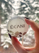 Hand holding a round container of Écani cream with a blurred natural grass-fed beef tallow face cream in jar background
