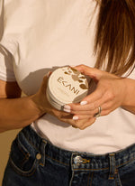 Person holding a container with 'Ecani' branding Ecani all natural whipped tallow cream container with cow print design