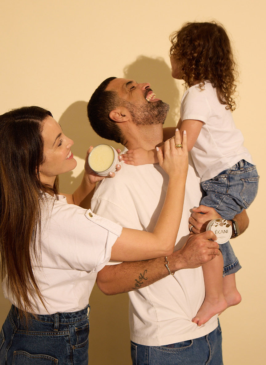 Family of three with a child on a man's shoulders against a beige background using tallow grass-fed cream