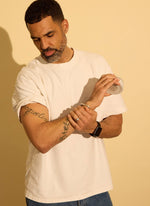 Man in a white t-shirt holding a grass-fed beef tallow face cream in tin jar against a beige background